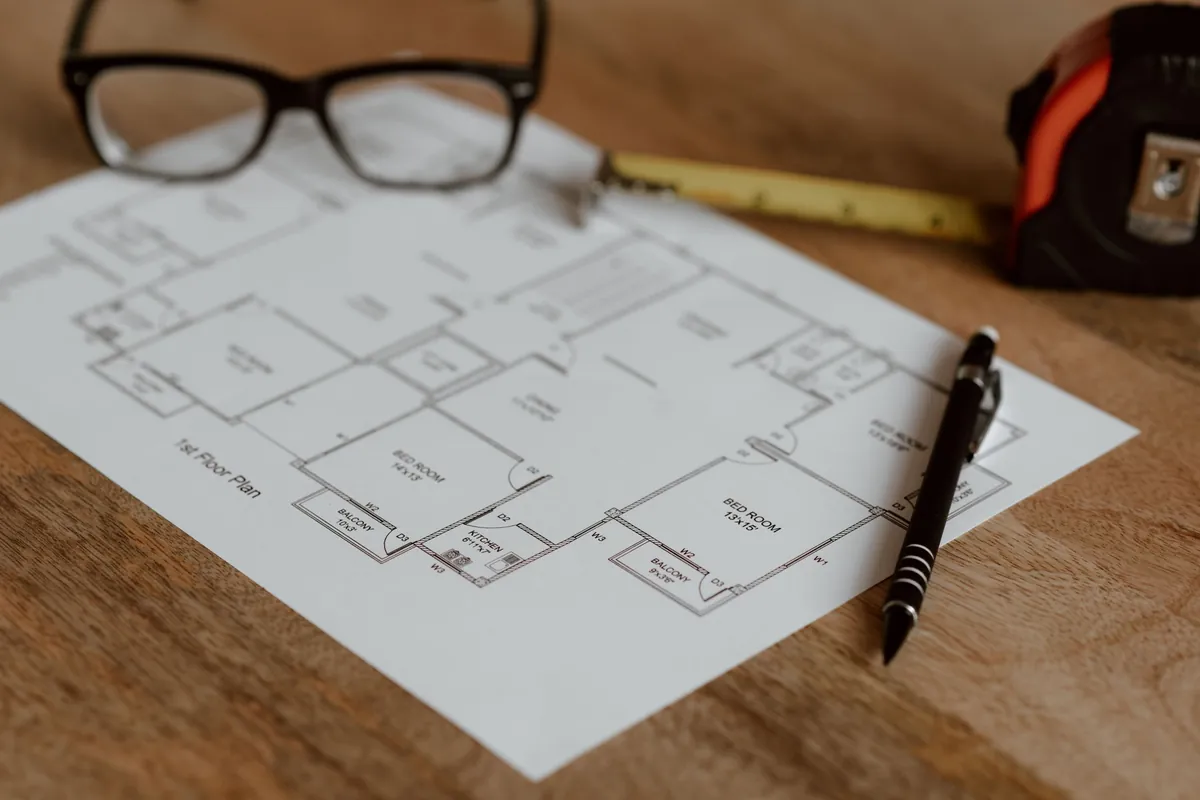Pool and home plans on a desk with glasses, pen and tape measure