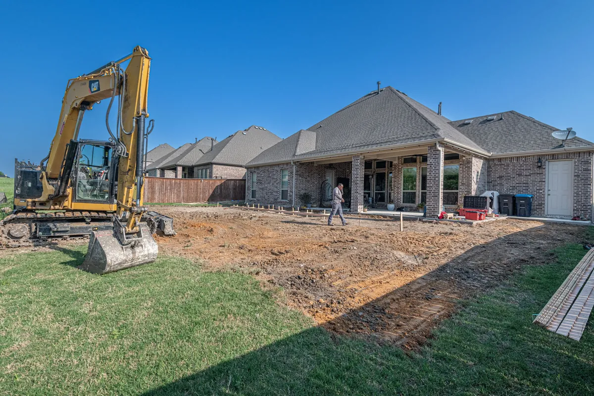 Excavator digging out a new backyard behind a brick home