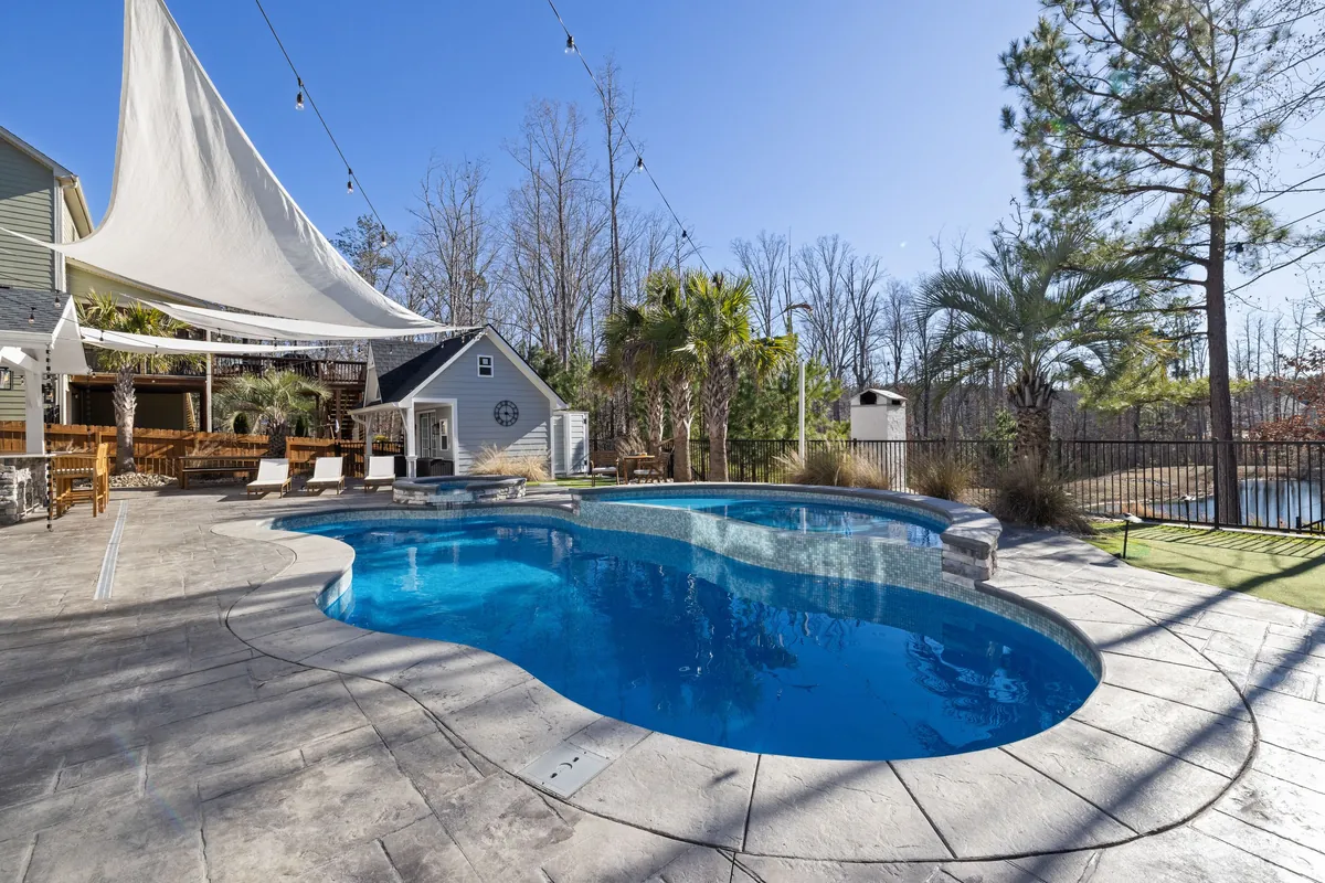 Finished freeform pool with a raised spillover spa and stamped concrete deck